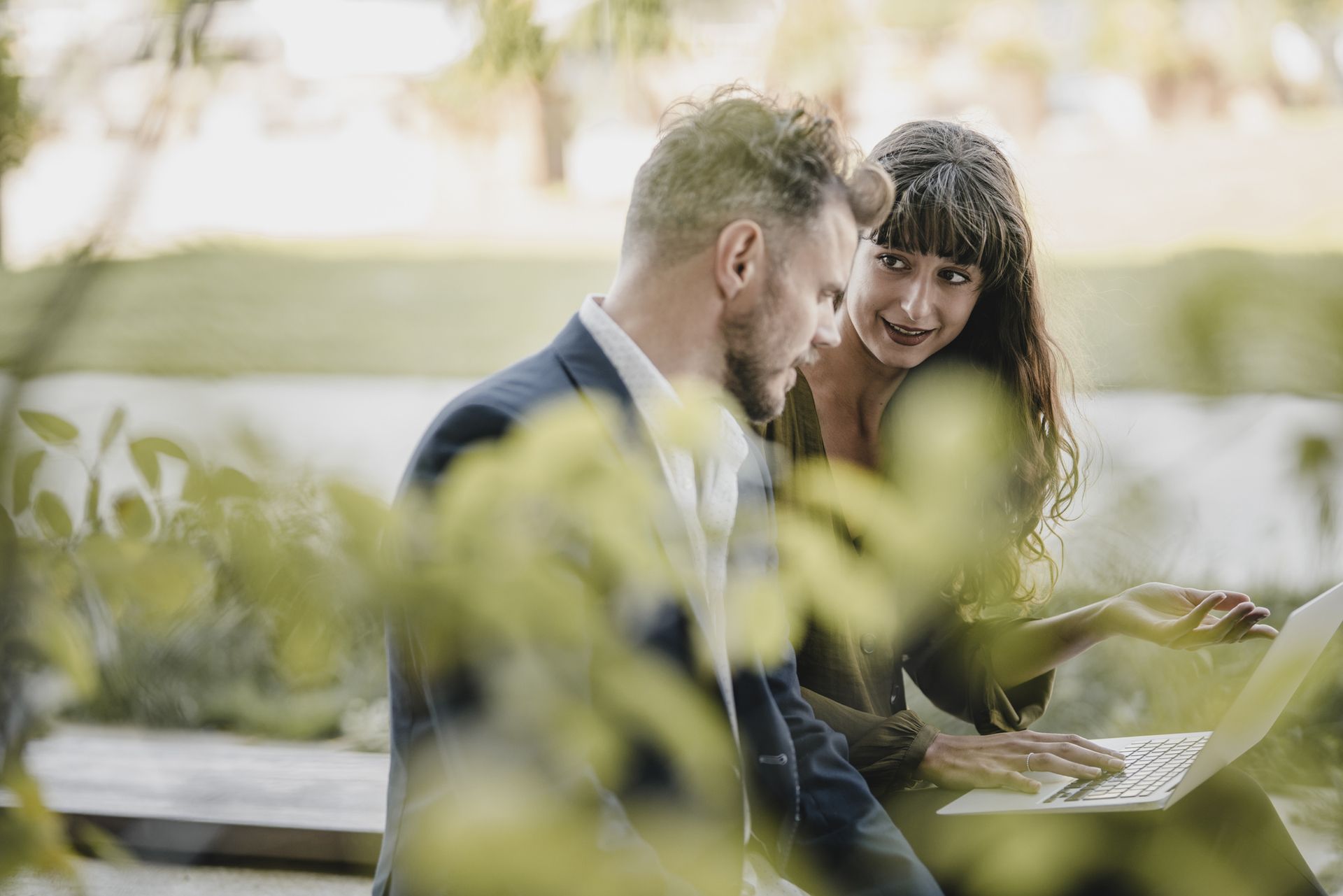 Muž a žena si společně prohlížejí udržitelná technologická řešení na notebooku v přírodě.